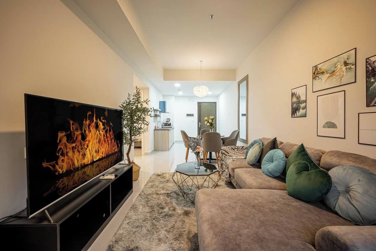 En moderne stue med et fladskærms-tv, en sofa, et sofabord og et spiseområde i baggrunden.