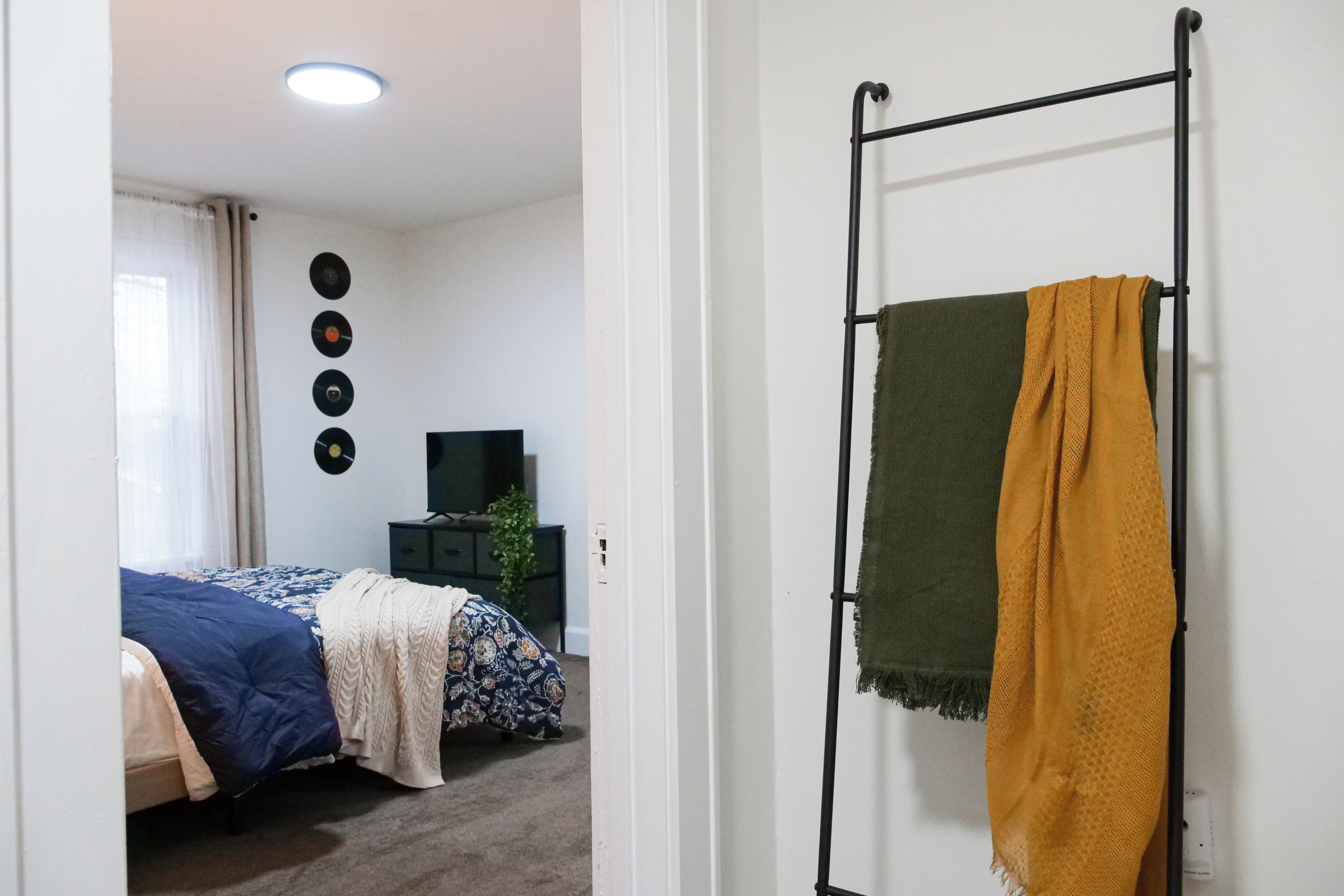 A bedroom with a bed, a TV, a wall-mounted record player, and a towel rack with two towels.