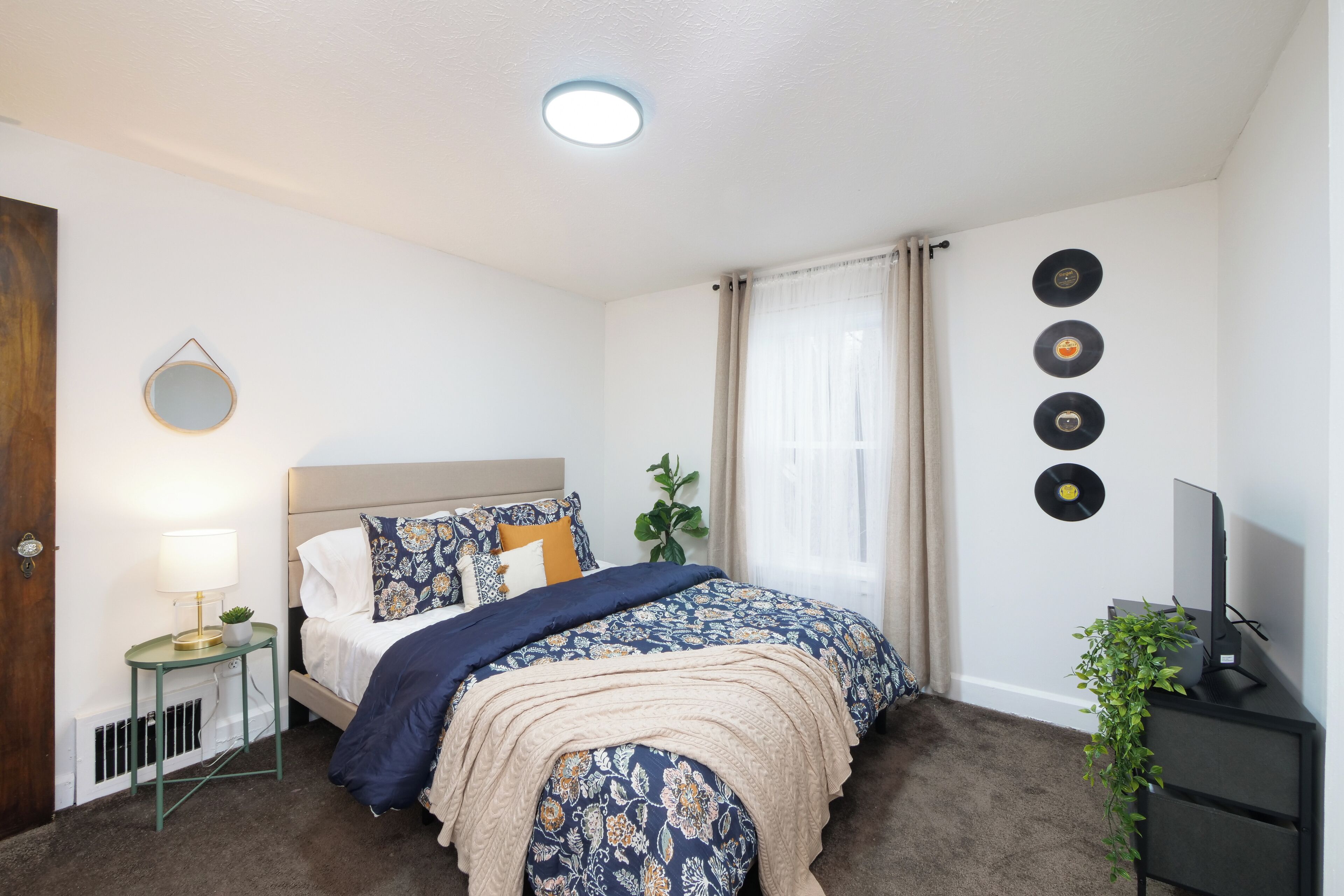 A bedroom with a bed, bedside table, lamp, and wall decorations including vinyl records.