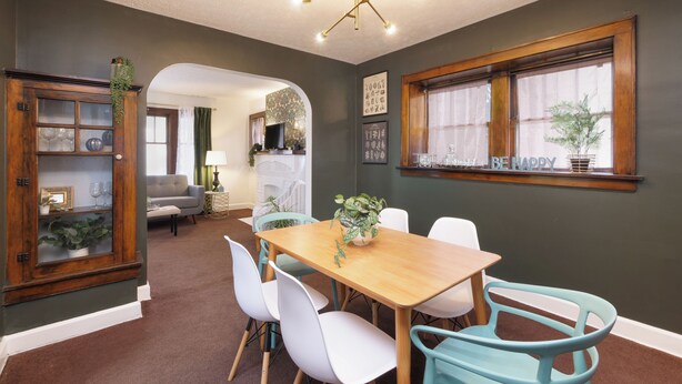 A dining area with a wooden table and white chairs, a cabinet with glass doors, and a window with curtains. - Renovated 3BR Family Retreat, Sleeps 8 - Dog-Friendly (Akron)