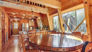 Un interno in legno con un tavolo rotondo circondato da sedie, un angolo cottura e ampie finestre.