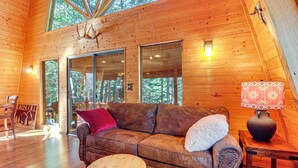 Interno di una baita in legno con un divano in pelle, un tavolino rotondo in legno e una lampada su un comodino.