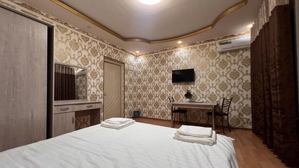 A hotel room with a bed, a desk, a chair, a TV, and a wardrobe.