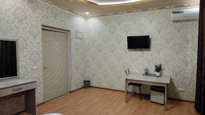 A room with patterned wallpaper, a desk with chairs, a television, and an air conditioning unit.