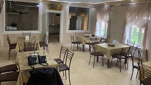 A dining area with multiple tables and chairs, a kitchen visible through an open doorway, and a brick wall.
