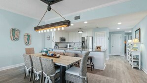 A modern kitchen with white cabinets, a central island, and a dining area with wicker chairs.