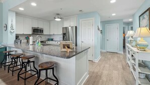 A modern kitchen with white cabinets, granite countertops, and stainless steel appliances. There are bar stools and a small island with a sink.