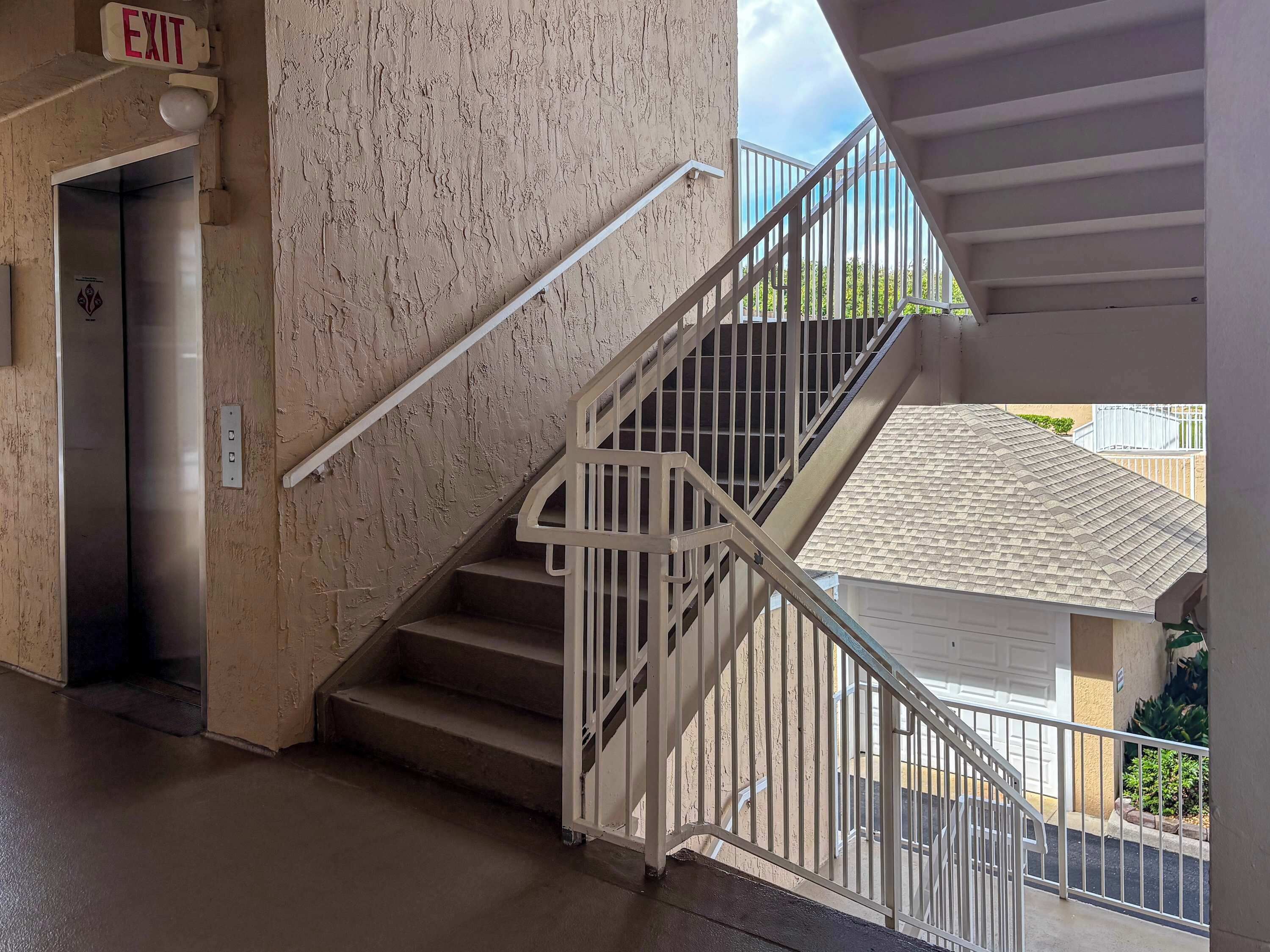A staircase with a handrail, an exit sign, and an elevator door.