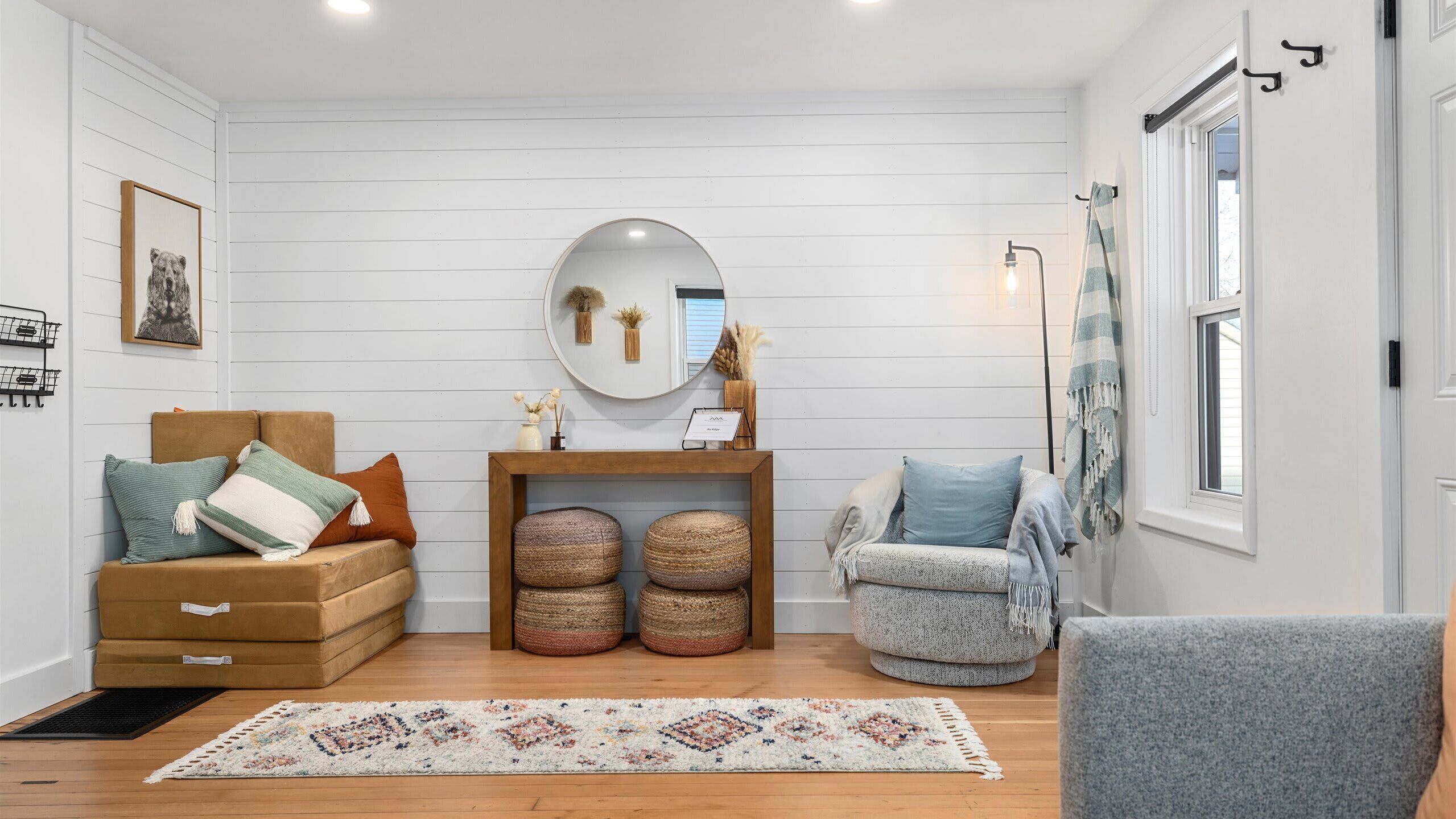 A cozy living room with a brown sofa, a grey armchair, and a round mirror above a wooden console table.