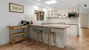 Une cuisine moderne avec des meubles blancs, un îlot central doté de tabourets, un four à micro-ondes et un extincteur visible.