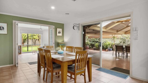 Un coin repas avec une table et des chaises en bois, une vue sur le jardin à travers des portes vitrées et une horloge au mur.