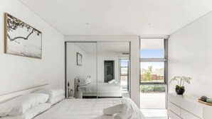 Un dormitorio moderno con una cama grande, un vestidor y un ventanal corredero que da a un balcón.