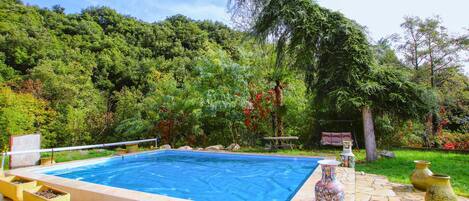 Una piscina con un patio circundante, una silla colgante y jarrones decorativos.