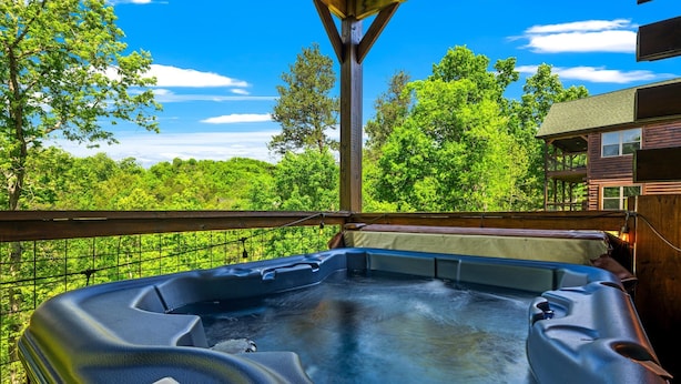 Un bain à remous doté d’un panneau de commande, entouré d’une terrasse en bois et offrant une vue sur une zone boisée.