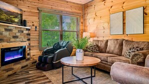 Une pièce chaleureuse avec une cheminée en pierre, un fauteuil massant, un canapé et un mur en bois.