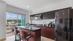 A modern kitchen with dark wood cabinets, a stainless steel refrigerator, a built-in microwave, and a large island with bar stools.