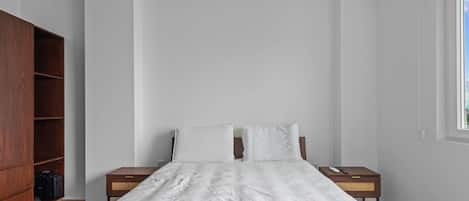 A bedroom with a bed, two nightstands, a wooden wardrobe, and a window.