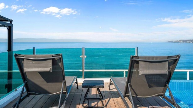 A deck with two chairs and a small table, overlooking a clear blue sea and distant land.