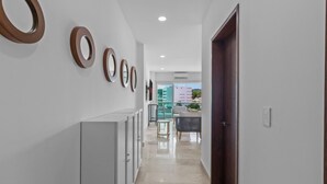 A hallway with a series of circular mirrors on the wall, a grey cabinet, and a wooden door leading to a balcony with a view of buildings and greenery.