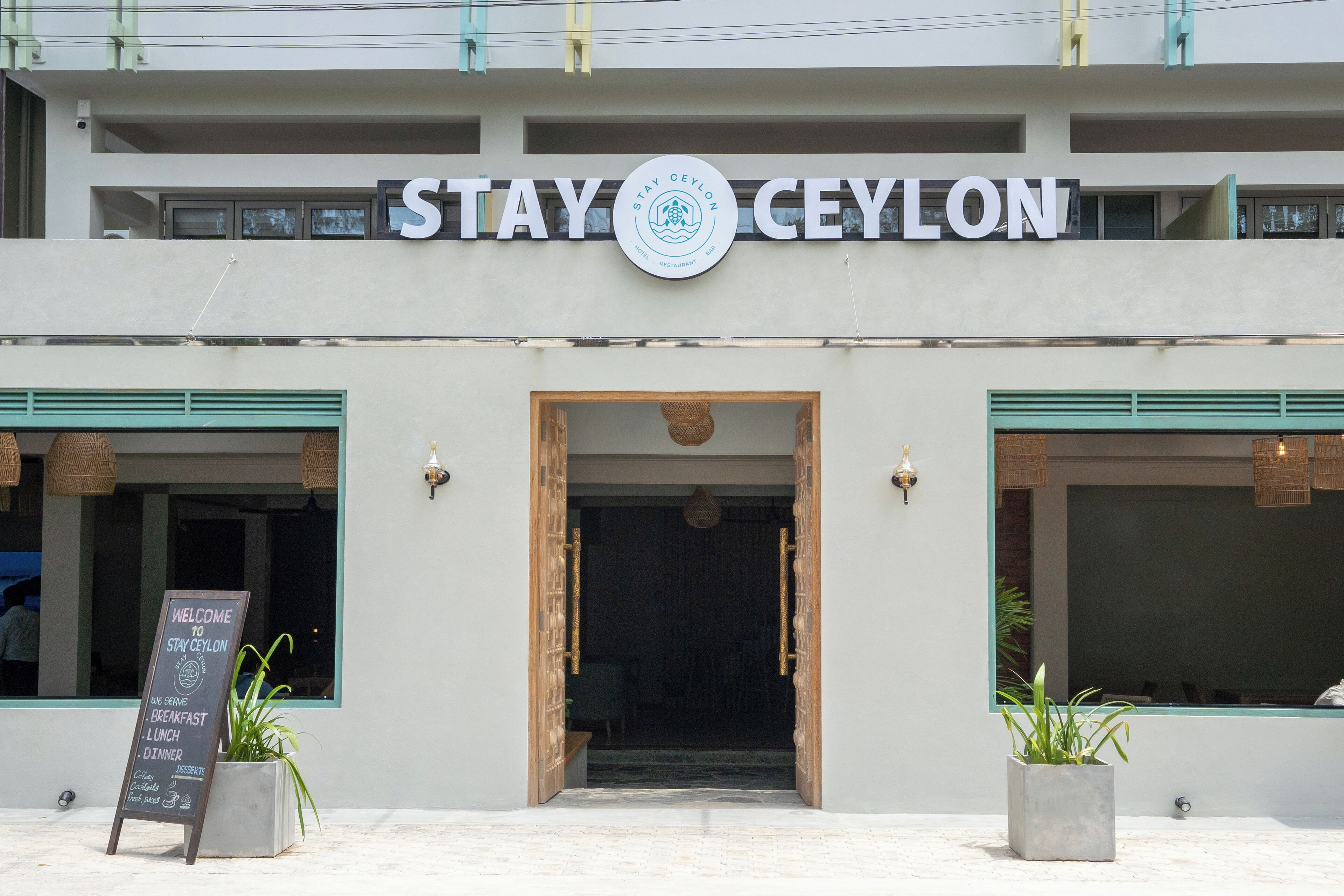 A hotel entrance with a sign reading 'STAY Ceylon' and a welcome sign listing breakfast, lunch, dinner, and desserts.