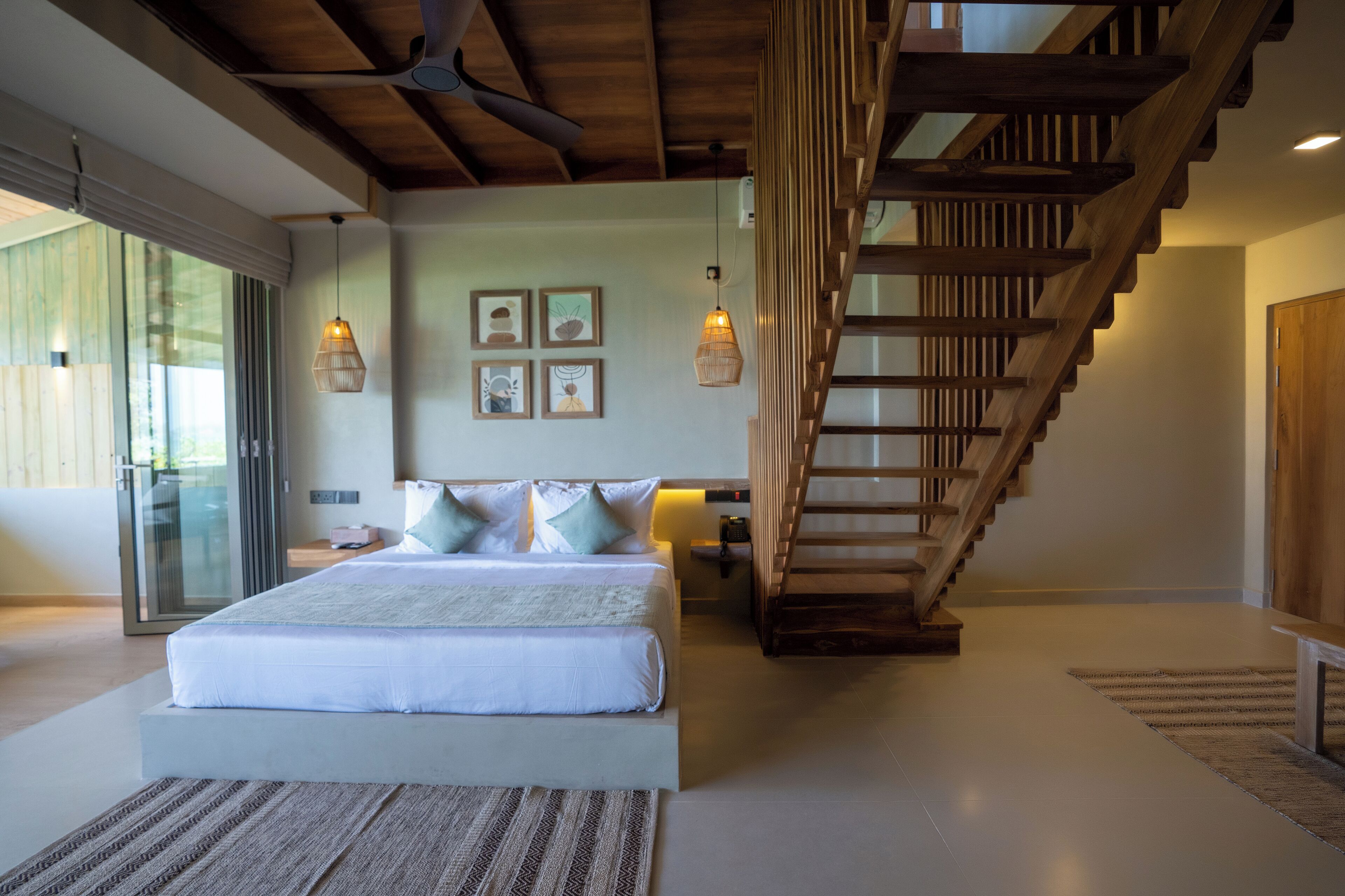 A bedroom with a large bed, a wooden staircase, and a sliding glass door.