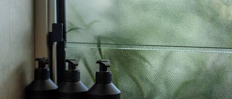 Three black bottles labeled 'Shower Gel,' 'Shampoo,' and 'Conditioner' on a windowsill.