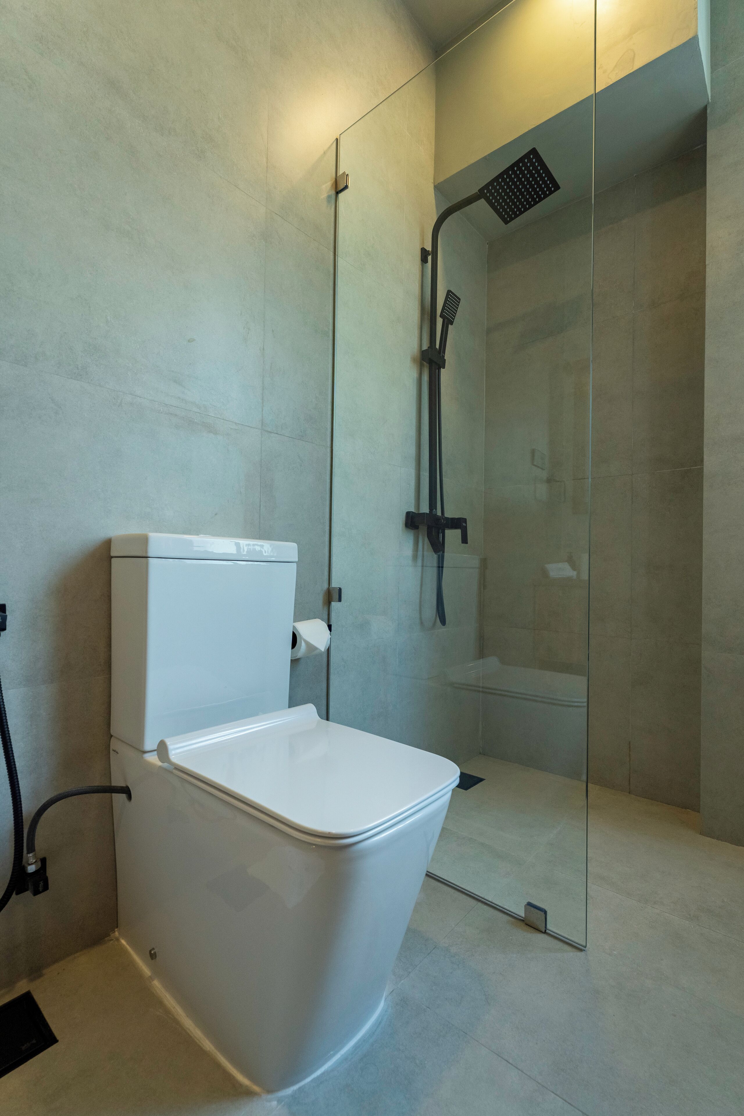 A modern bathroom with a toilet, a glass-enclosed shower, and a visible toilet paper holder.