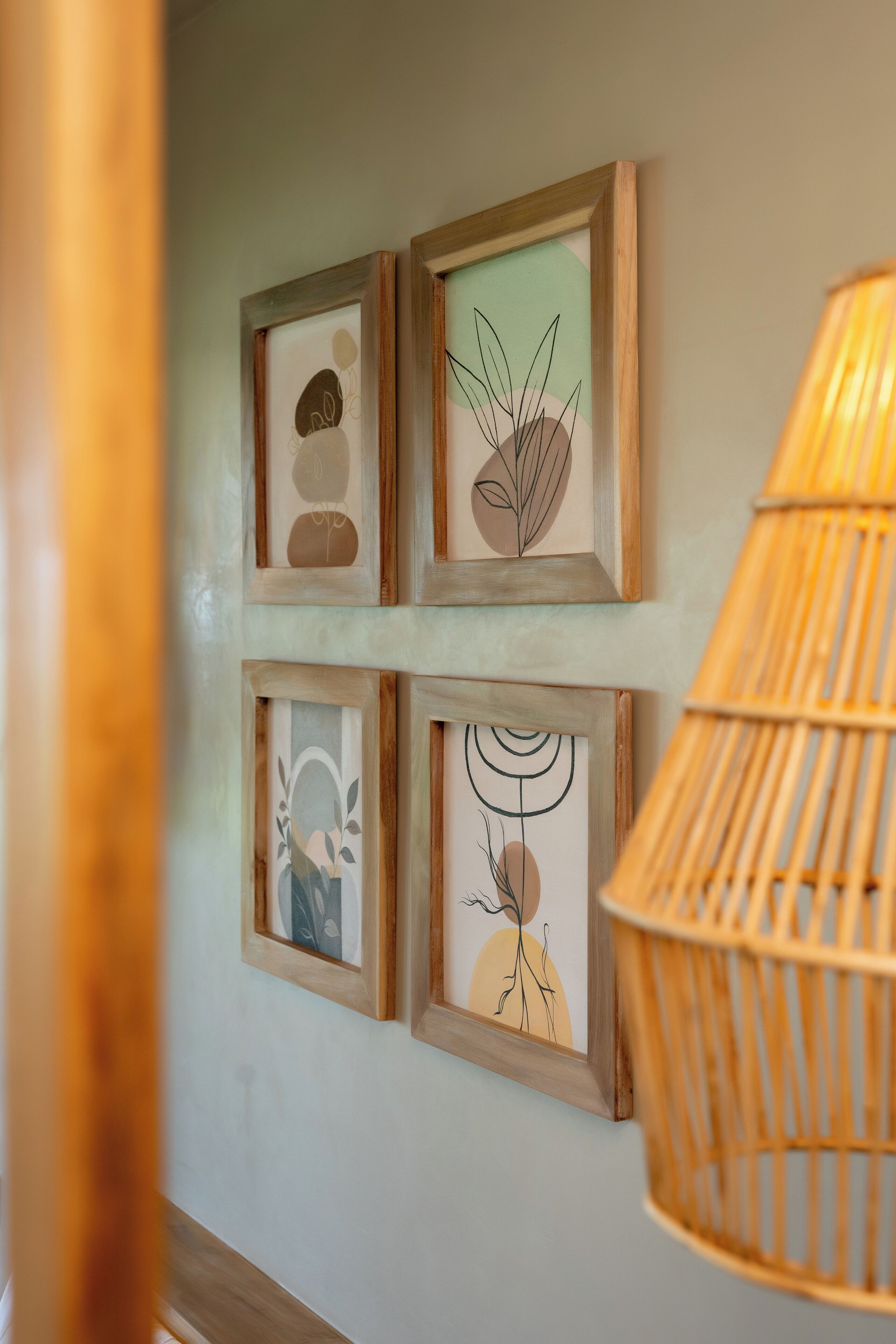 A wall with four framed artworks and a wicker lamp.