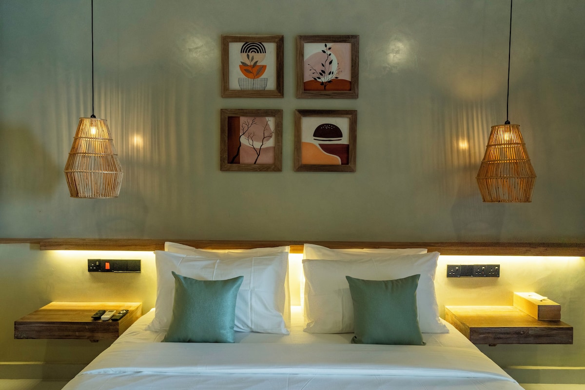 A hotel room with a bed, bedside tables, wall-mounted artwork, and hanging lamps.