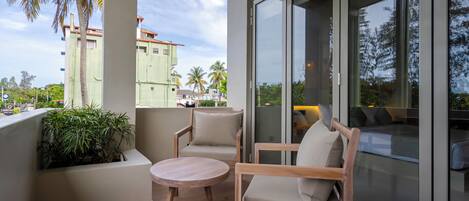 A balcony with two wooden chairs and a small round table, overlooking a cityscape with palm trees and buildings.