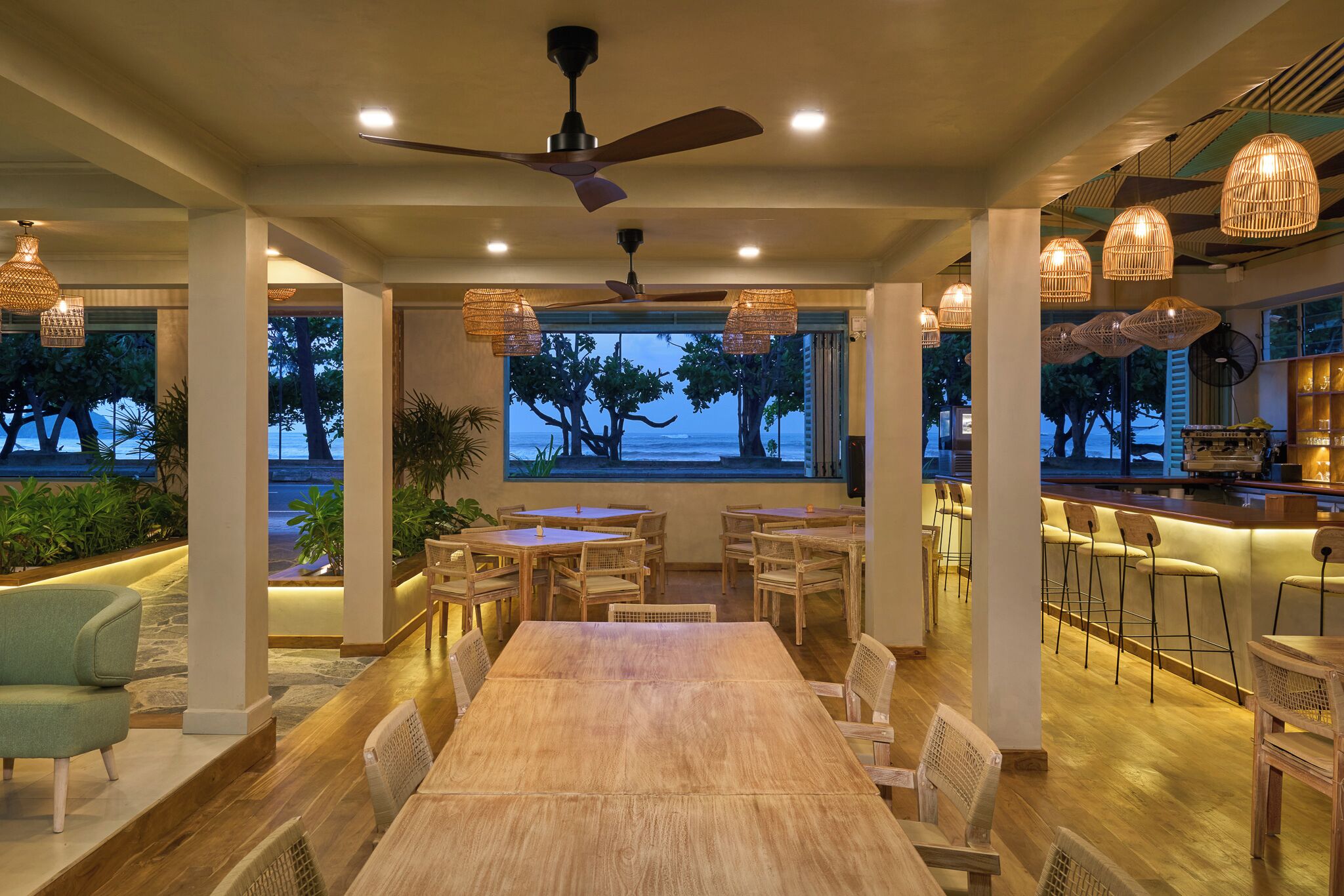A spacious dining area with a large wooden table and chairs, surrounded by hanging wicker light fixtures and a ceiling fan.