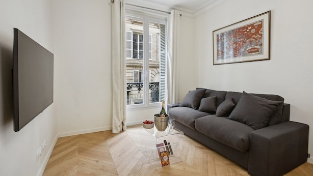 Una sala de estar moderna con un sofá gris, un televisor de pantalla plana, una ventana con cortinas blancas y un mapa enmarcado en la pared.