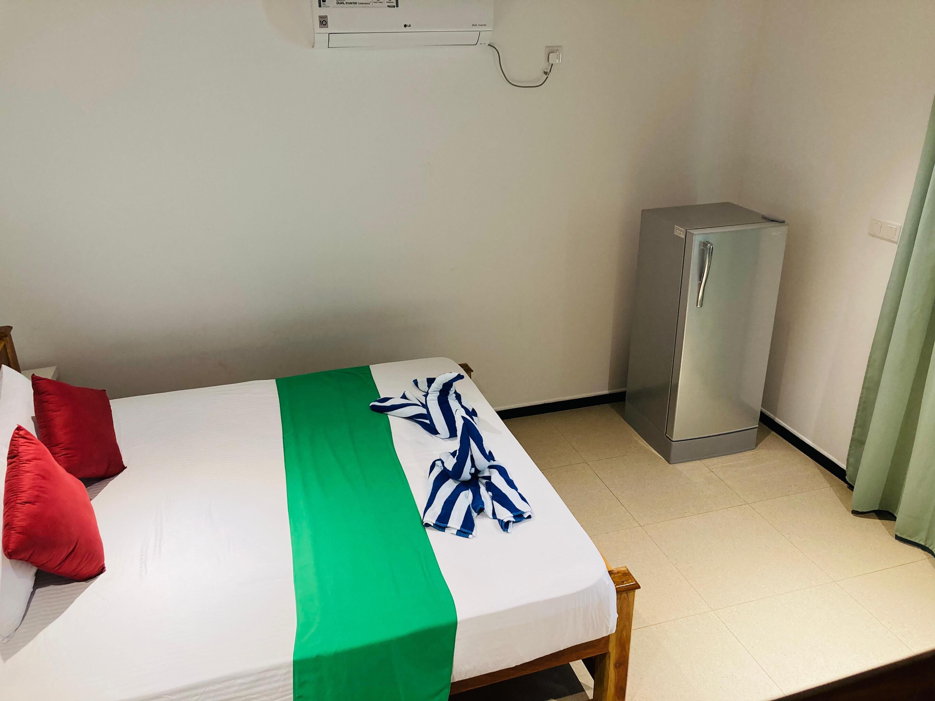Een kamer met een bed, een klein kastje en een luchtverkoeler aan de muur.