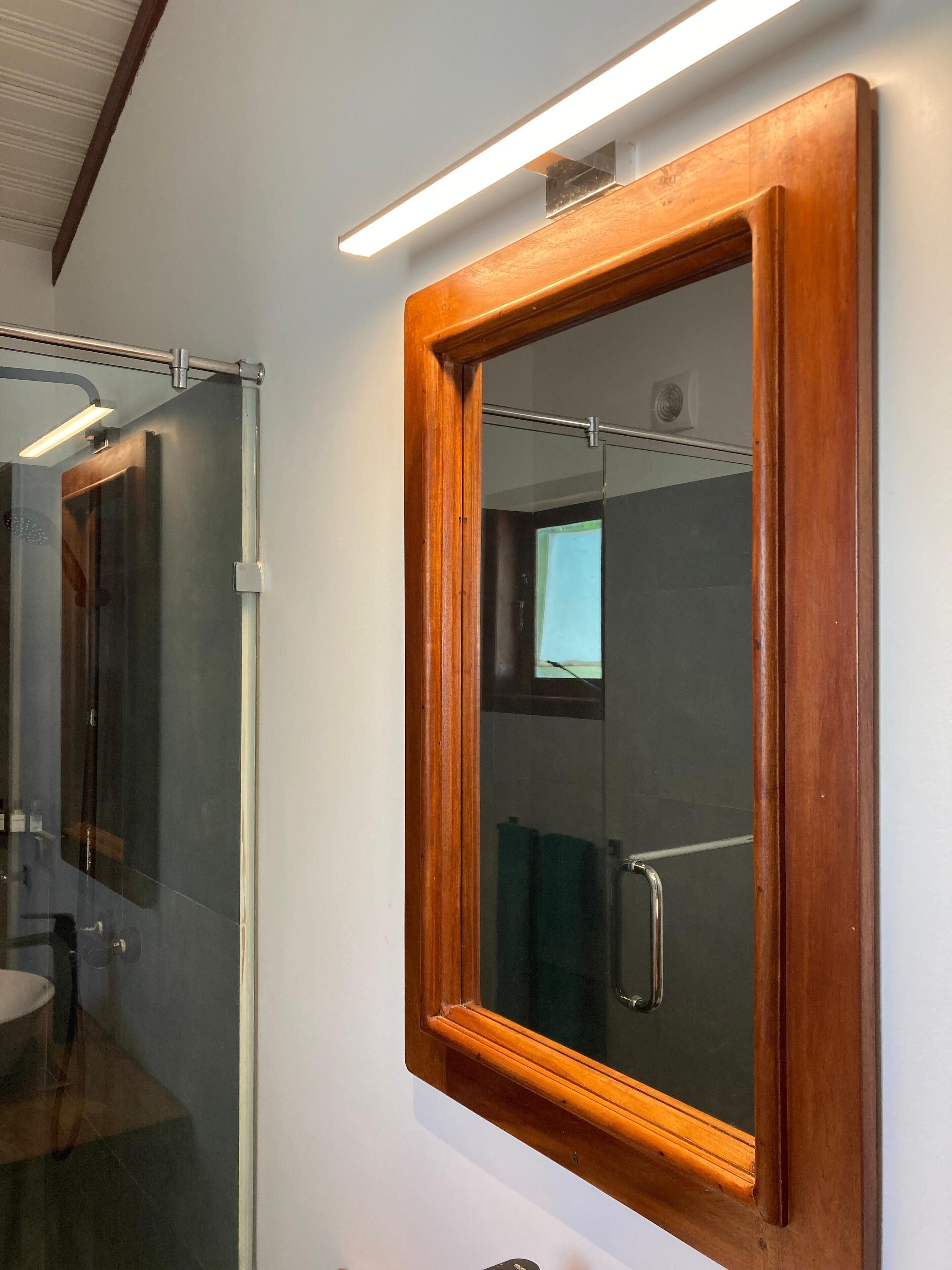 A bathroom with a wooden-framed mirror, a glass shower enclosure, and a visible toilet.