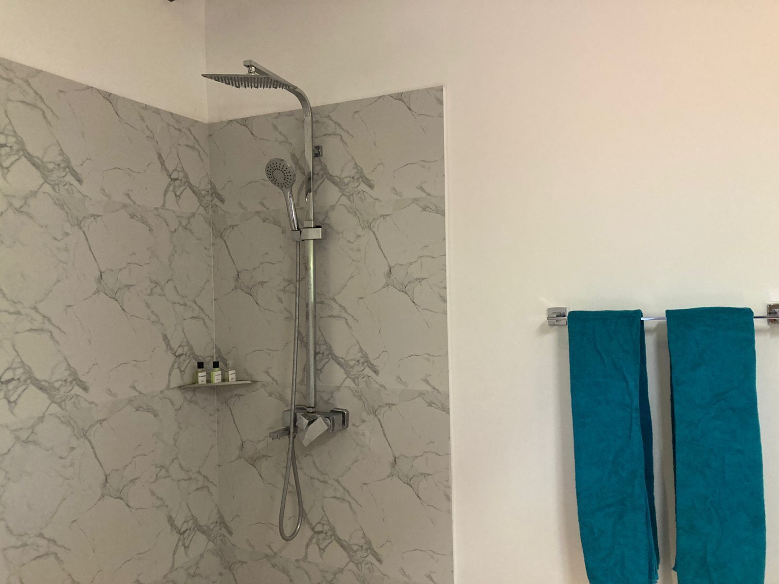 Un baño con ducha, paredes de mármol y dos toallas colgadas en un perchero.
