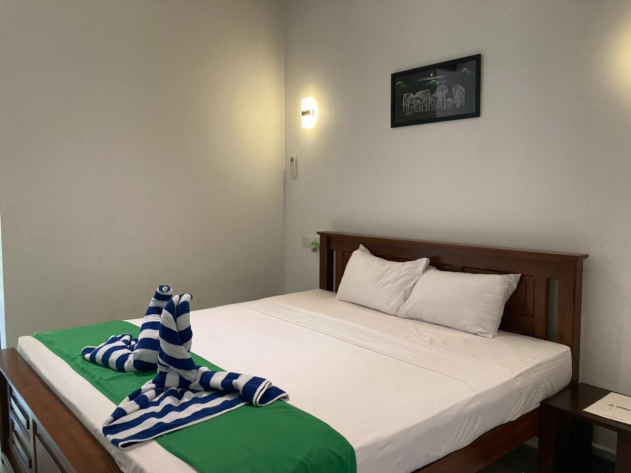 A neatly made bed with a green and white striped blanket, a wooden headboard, and a framed picture on the wall.