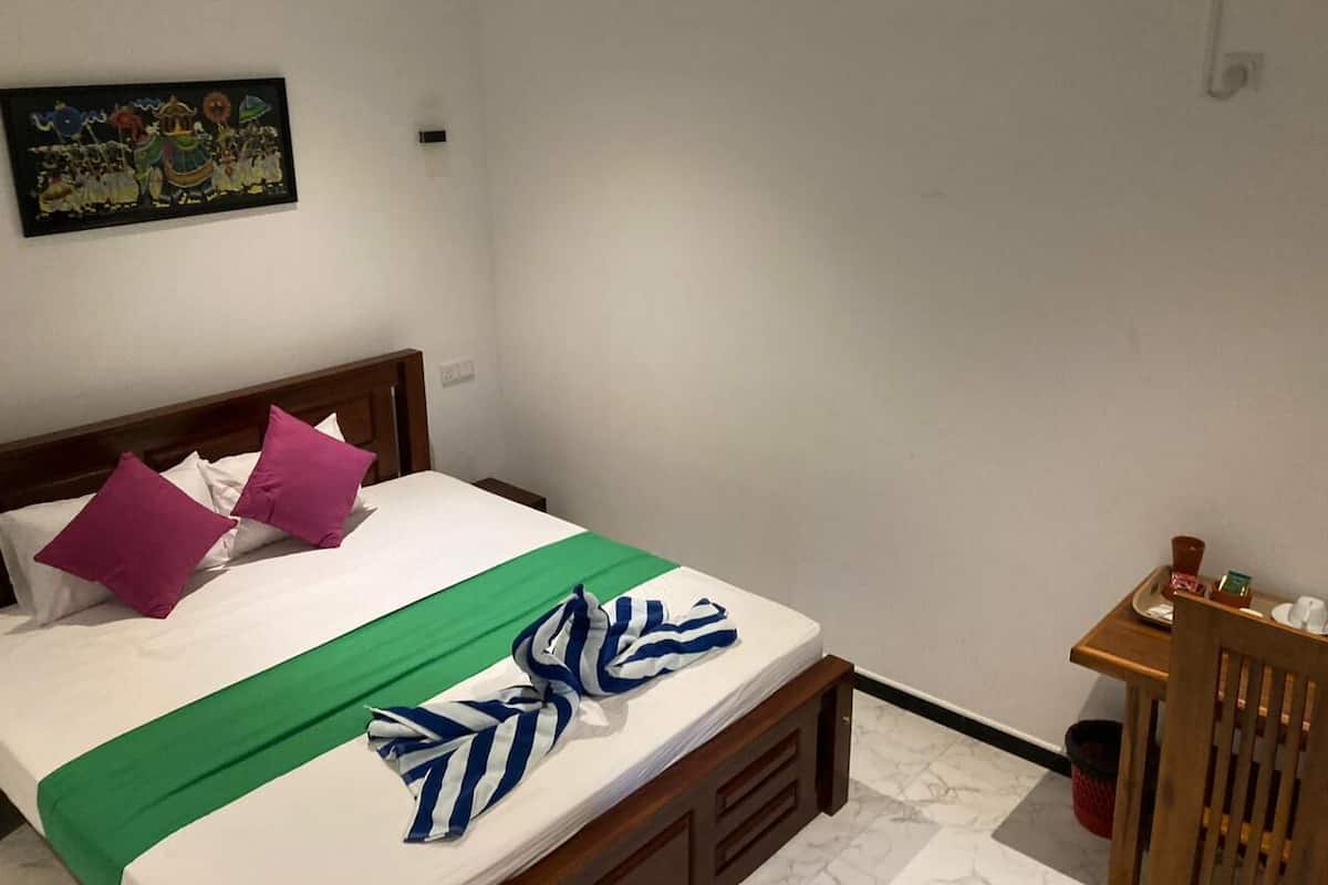 Un lit bien fait, avec une couverture verte, deux coussins violets et une serviette à rayures.