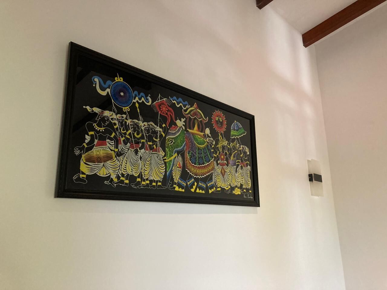 Une œuvre d’art encadrée représentant une scène colorée avec des personnages et des animaux sur un mur.