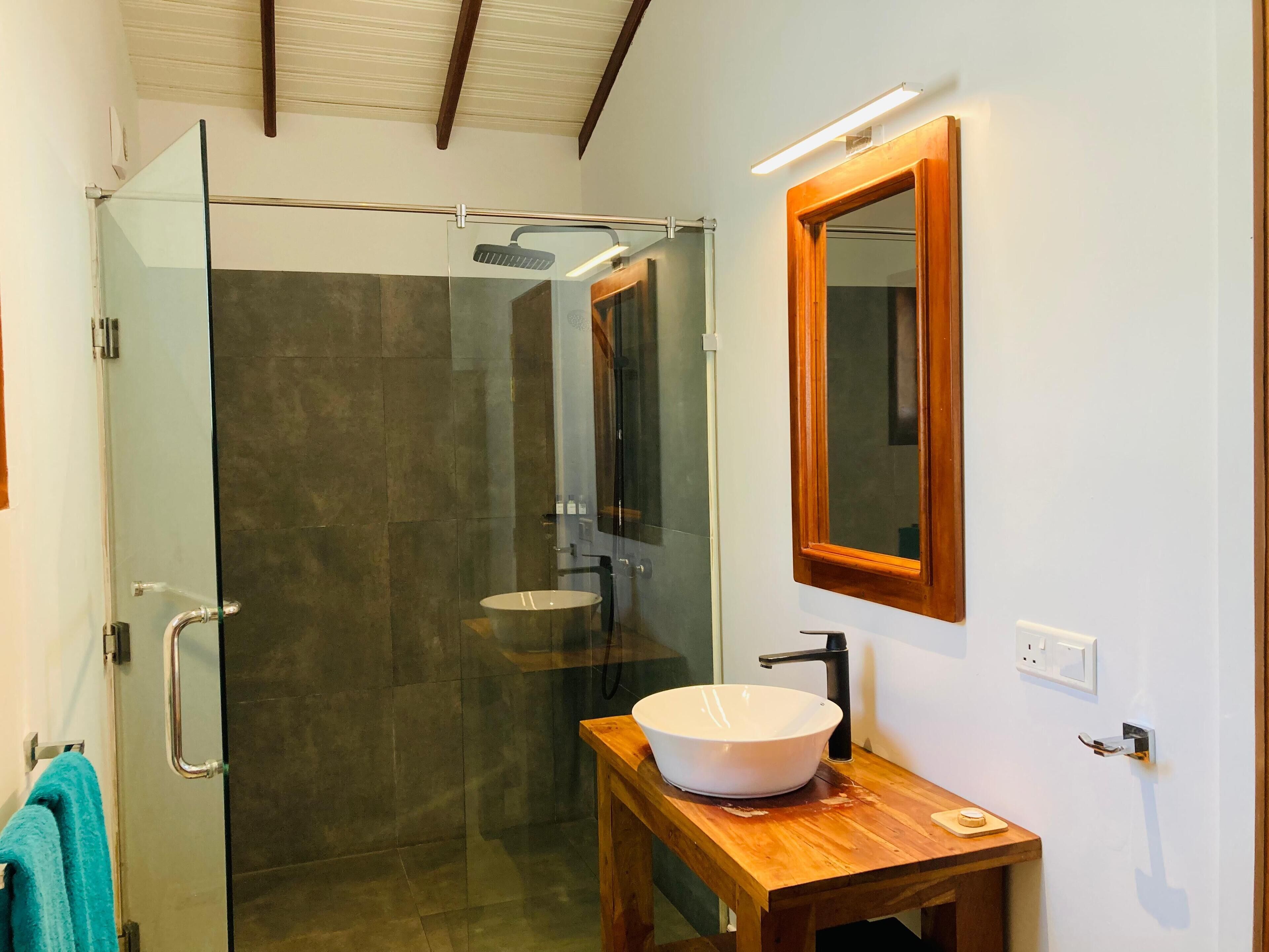 Un baño moderno con cabina de ducha de vidrio, tocador de madera con lavabo blanco y espejo sobre el tocador.