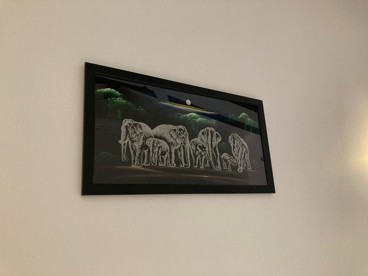 Ein gerahmtes Kunstwerk mit Elefanten und Mond an einer Wand.