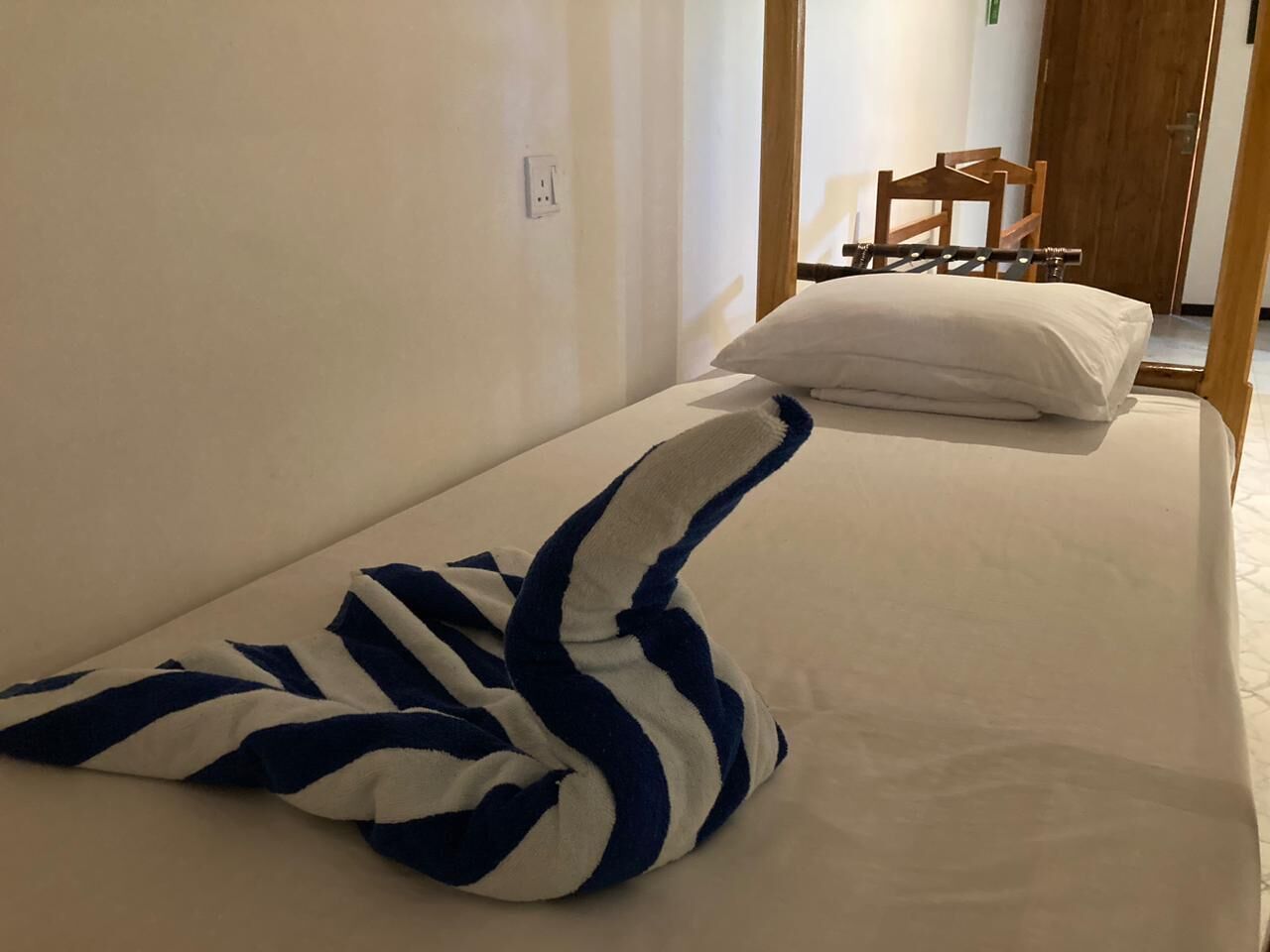 Uma cama de solteiro com travesseiro branco e toalha listrada.