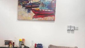 Una habitación con un sillón color beige, una mesita consola de metal negro con objetos encima, y un cuadro de barcos en la pared.