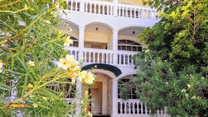 Un edificio de dos pisos con fachada blanca, varios balcones y una entrada central con arco.