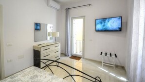Une chambre à coucher comprenant un lit, une commode, un téléviseur fixé au mur et une fenêtre avec des rideaux.