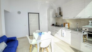 Une cuisine moderne avec des meubles blancs, un coin repas doté d’une table et de chaises blanches, et un canapé bleu.
