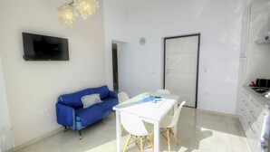 Un salon moderne avec un canapé bleu, une table à manger blanche et un téléviseur fixé au mur.