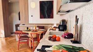 A modern kitchen with a wooden dining table, a coffee machine, and fresh vegetables on the counter. - Luxury Apartment - 2 bedrooms (Nice)