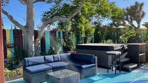 Un espace patio avec un canapé bleu pour l’extérieur et une table basse, entouré d’une clôture en bois et de diverses plantes.