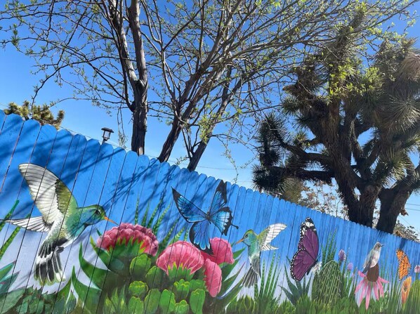 A mural of birds and flowers on a fence. - Artists in Wonderland: One-of-a-kind Vibrant Home (Yucca Valley)