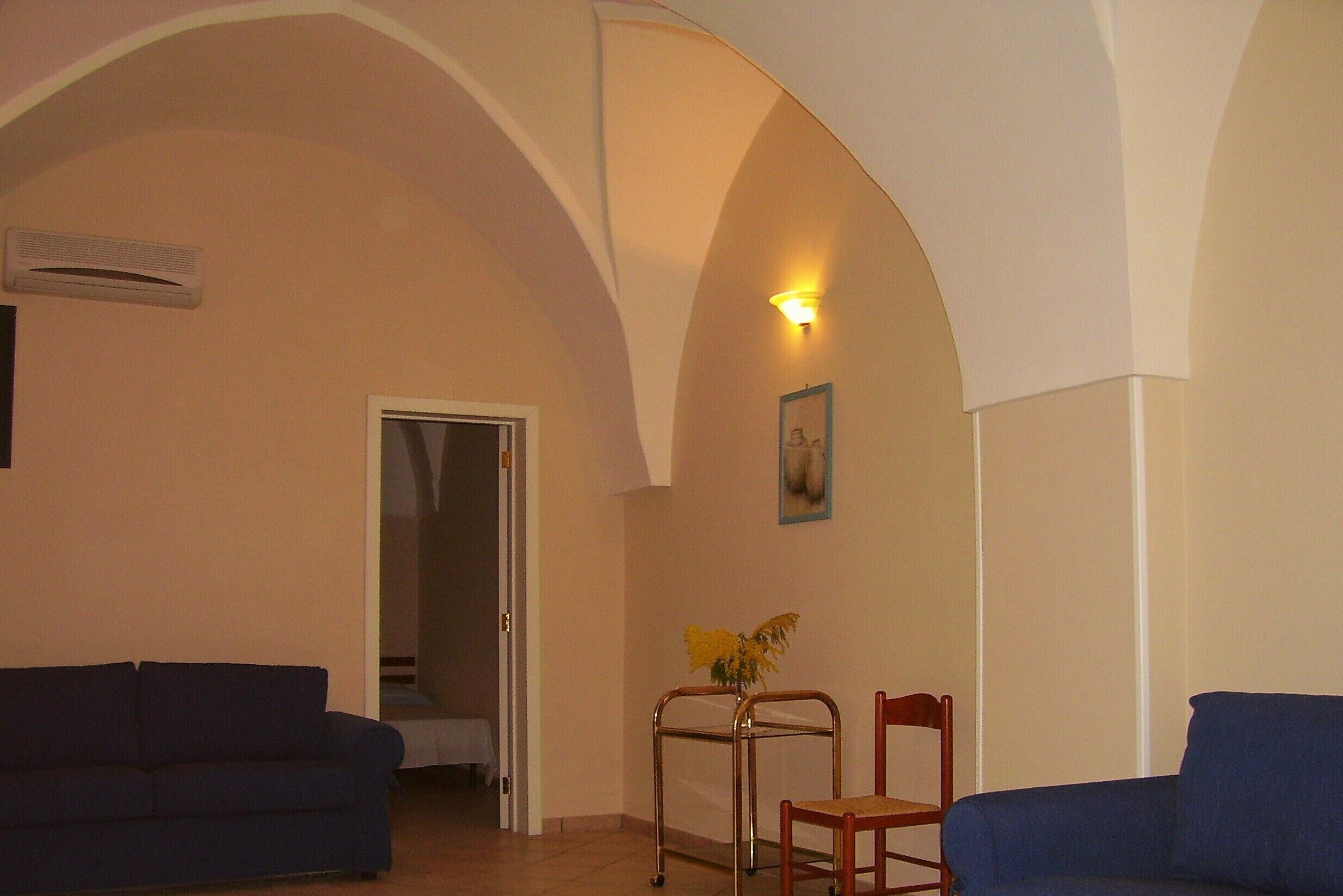 Ein Wohnzimmer mit zwei blauen Sofas, einem Metallstuhl, einem kleinen Tisch mit einer Vase und einer Tür zu einem anderen Raum.